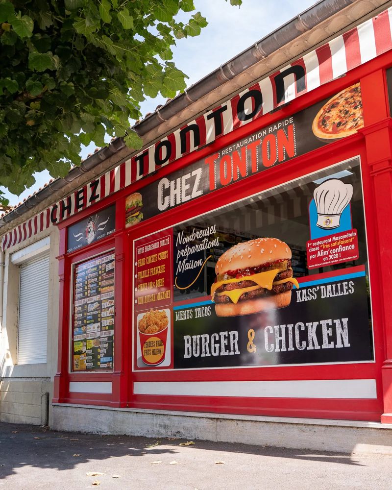 Devanture rouge et blanche de Chez Tonton vue de côté, avec la vitrine Burger et Chicken