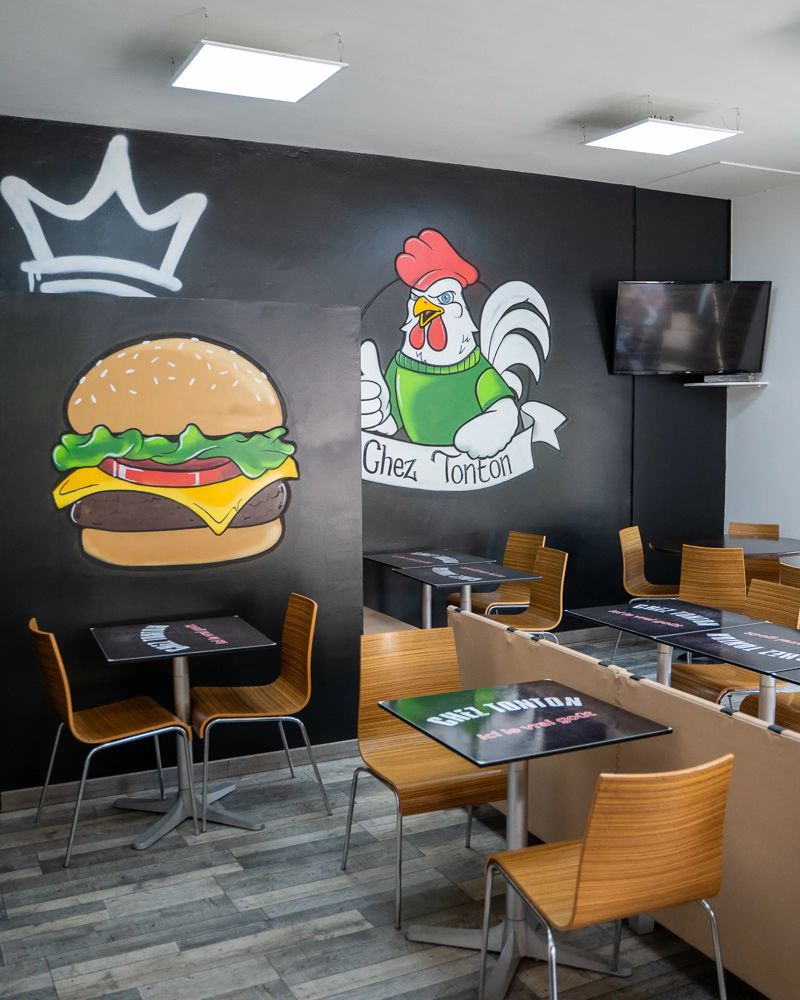 Salle de Chez Tonton avec la fresque du burger et du coq sur le mur noir